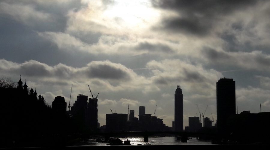 City Skyline in sillouhette with the sun shining through a cloudy sky reflected on the water
