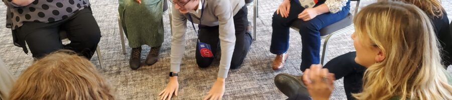 A man on all fours laughing surrounded by his laughing colleagues during a playful team away day